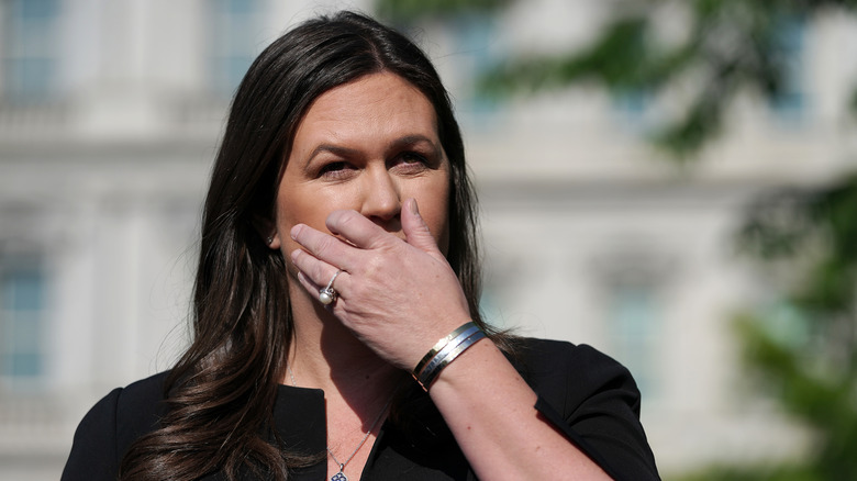 Sarah Huckabee Sanders covering her mouth in a black dress