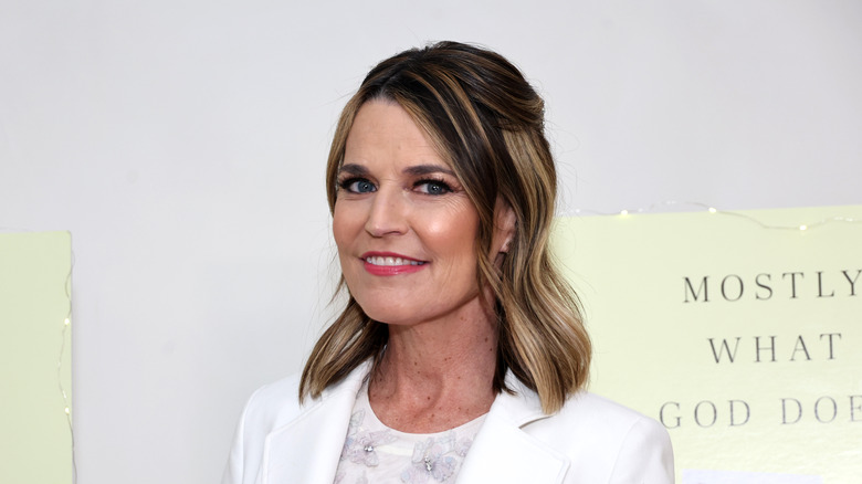 Savannah Guthrie smiling in a white suit at a book presentation of her book 'Mostly What God Does.'