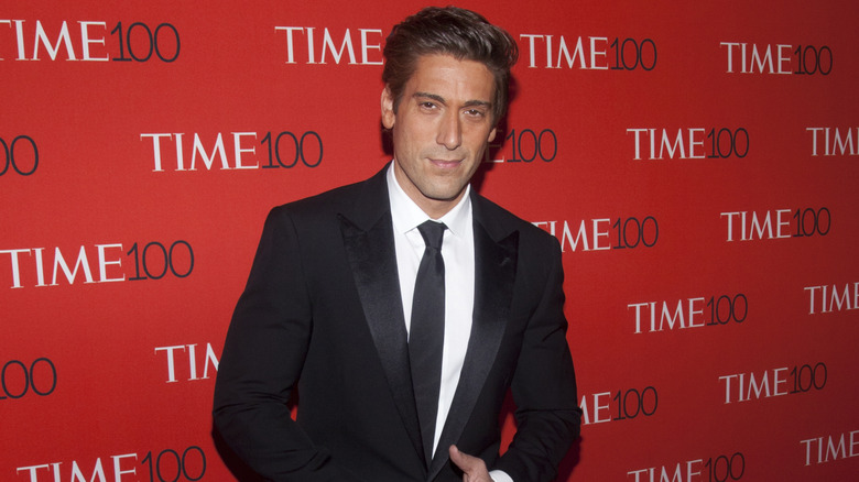 David Muir in a suit standing in front of red background.