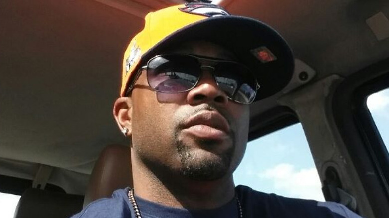 Keith Tisdell wearing a cap and a gold chain in a car