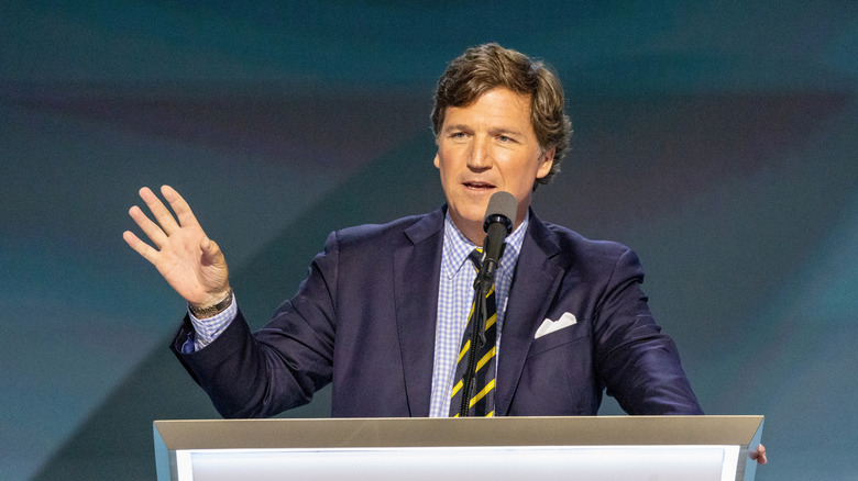 Tucker Carlson giving a speech with hand in the air