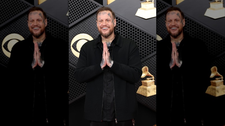 Jelly Roll smiling in a black shirt holding his hands together at his chest