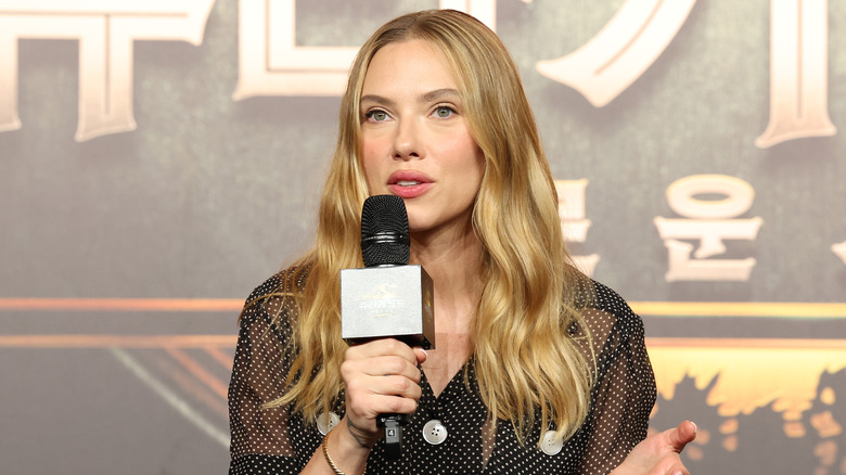 Scarlett Johansson speaking into a microphone in a black sheer top