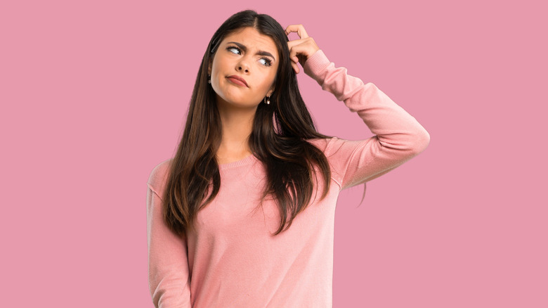 Woman in pink sweater scratching her head