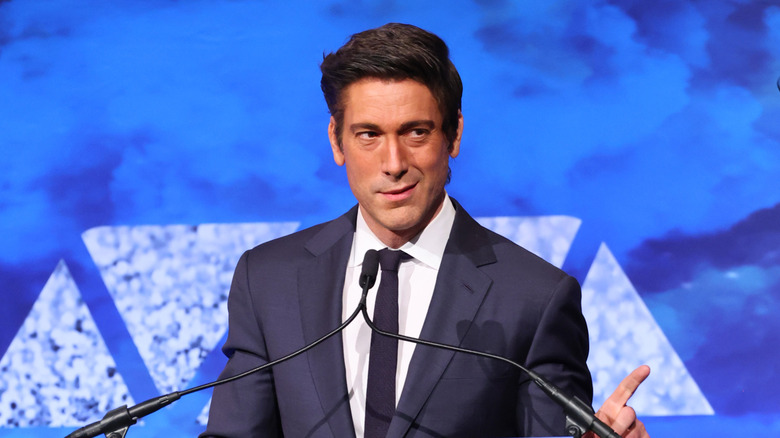 David Muir giving a speech at a podium and pointing one finger.