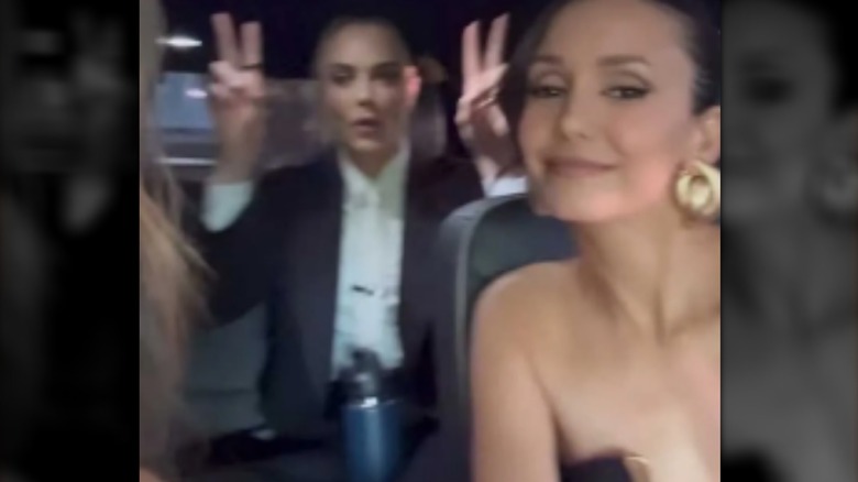 Cara Delevingne in the back seat of a car making peace signs, with Nina Dobrev smiling in the foreground.