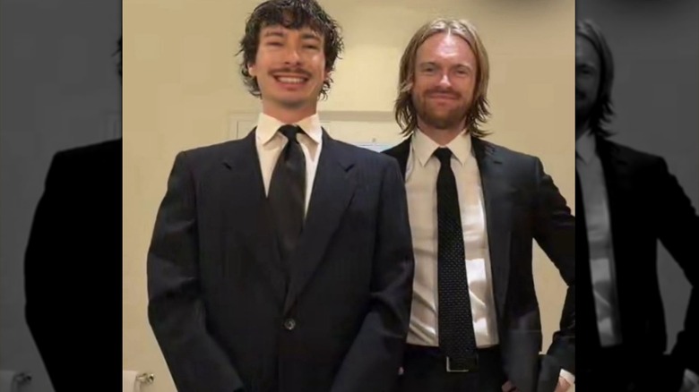 Finneas standing behind a friend, both smiling and wearing suits.