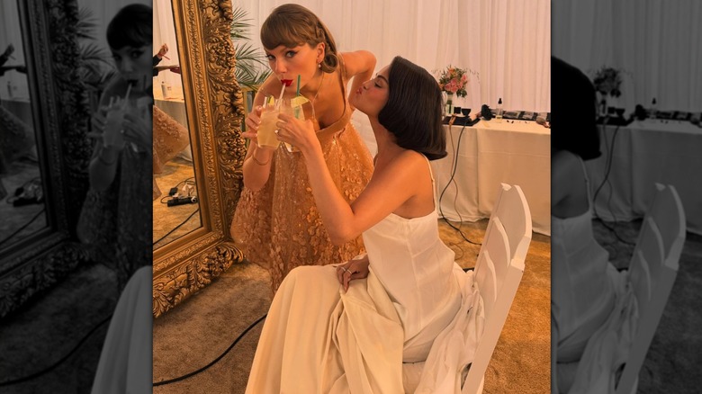 Taylor Swift, in a nude-colored gown, and Selena Gomez, in her wedding dress, cheersing with drinks.