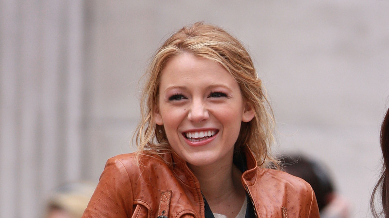 Blake Lively wearing a brown leather jacket and smiling.