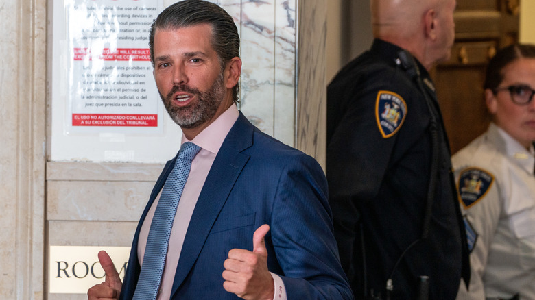 Donald Trump Jr. doing a double thumbs-up in a blue suit