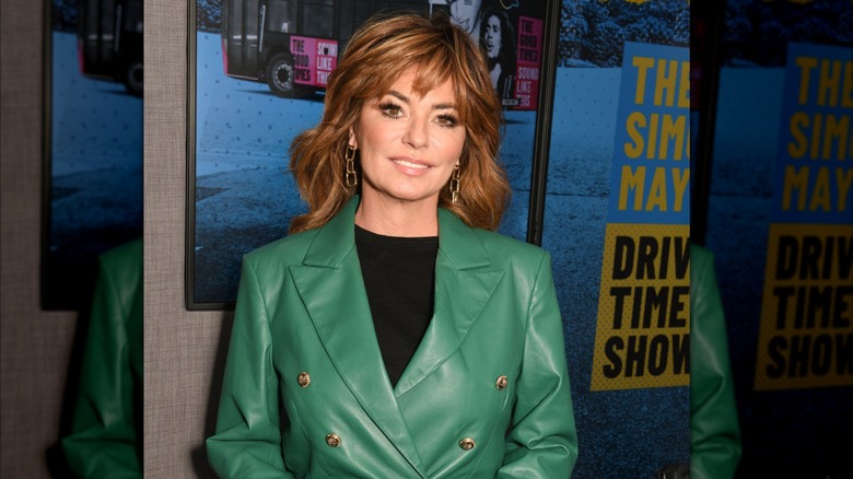 Shania Twain smiling while posing in a leather green suit jacket