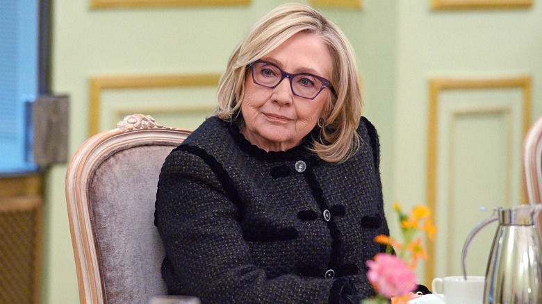 image of Hillary Clinton looking bored as she sits on a table