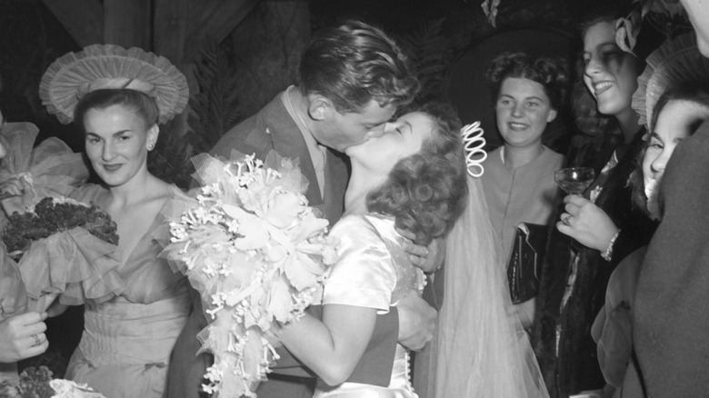 Shirley Temple and John Agar kissing while surrounded by guests at their wedding