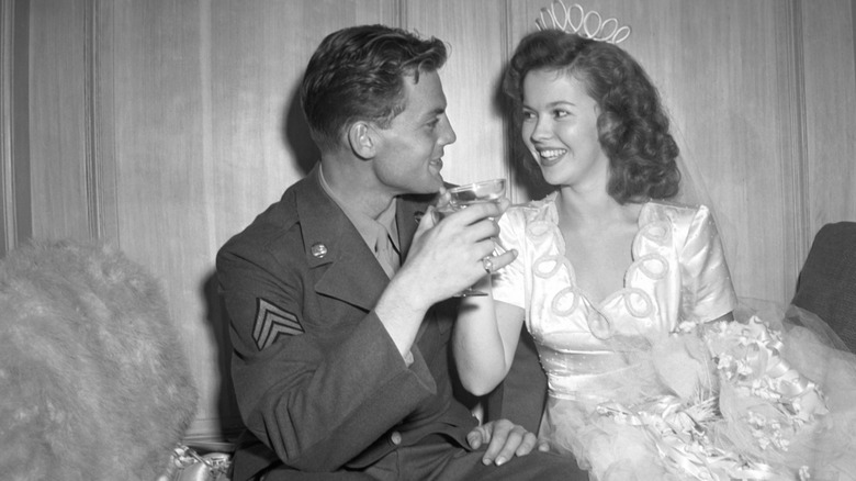 Shirley Temple and John Agar toasting at their wedding while sitting alongside each other
