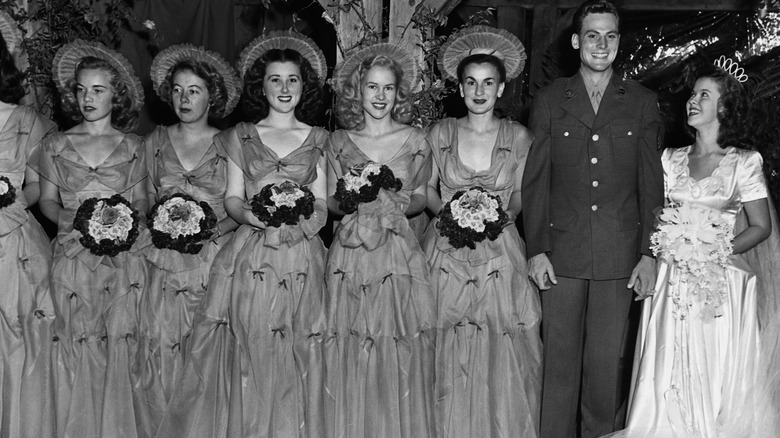 Shirley Temple gazes up at her husband, John Agar, while a row of bridesmaids stand alongside them