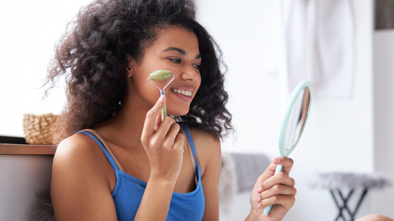 Young woman smiling while using a jade roller on her face