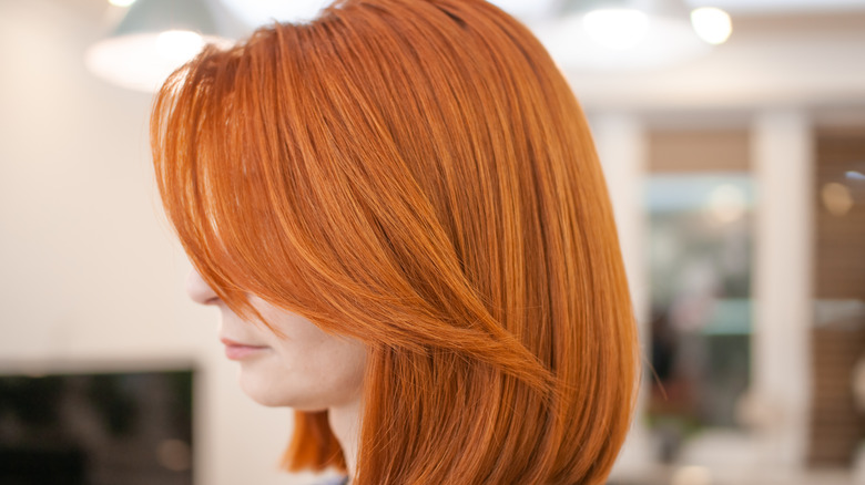 Woman with red hair getting a shoulder-grazing lob cut and side-swept bangs