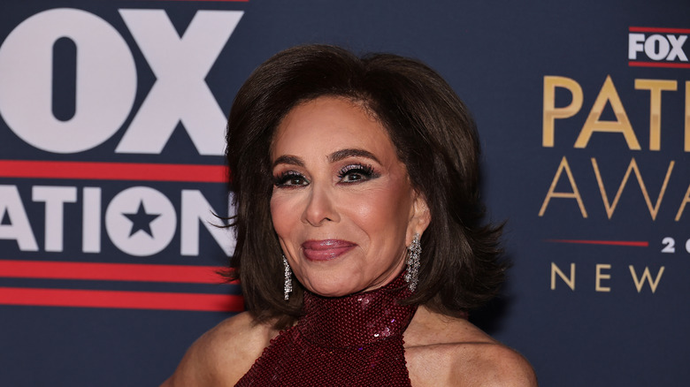 Jeanine Pirro posing at a Fox event in a sparkly purple dress with big poofy hair