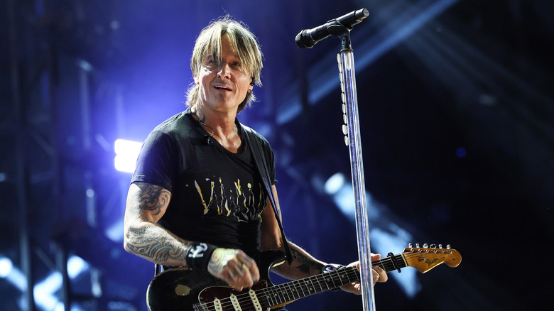Keith Urban wearing black and playing a guitar