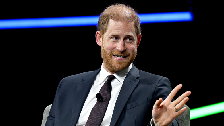 Prince Harry speaking while gesturing with his hand in a dark suit