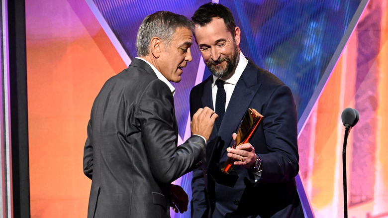 image of George Clooney and Noah Wyle leaning close to each other at the stage of an event
