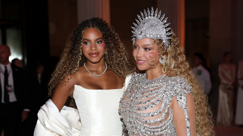 Beyoncé in a silver dress and matching headdress poses next to Blue Ivy Carter, who wears a white strapless dress, at the 2026 Met Gala.