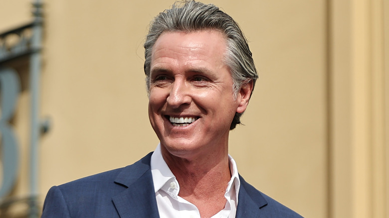 California Governor Gavin Newsom smiling in a grey suit jacket and open-collared white shirt