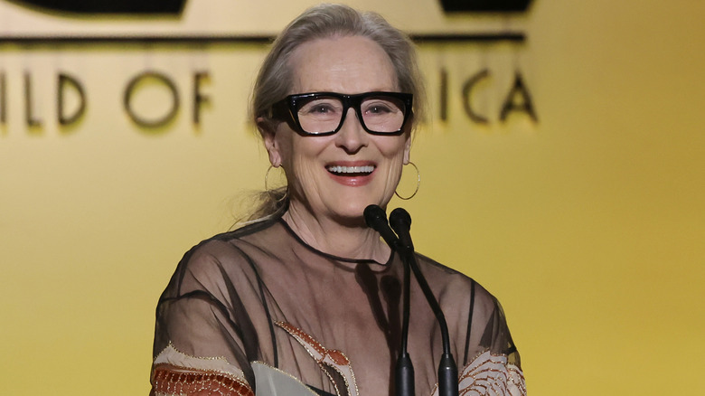image of Meryl Streep smiling mid-speech in front of a microphone