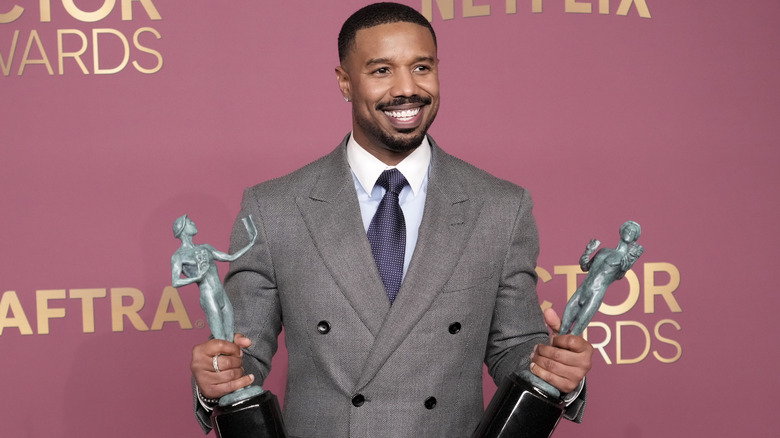 image of Michael B. Jordan smiling wide while holding two statues of his wins at the Actor Awards