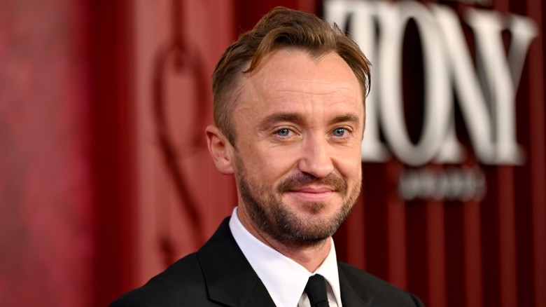 Tom Felton smiling in a suit while posing at an event