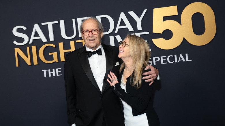image of Chevy Chase and Jayni Chase smiling and holding each other on the red carpet of SNL's 50th anniversary event