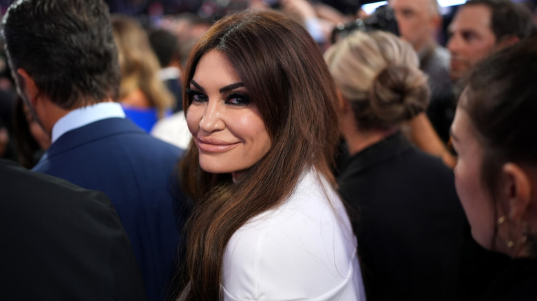 Kimberly Guilfoyle smiling while looking over her shoulder in a white top