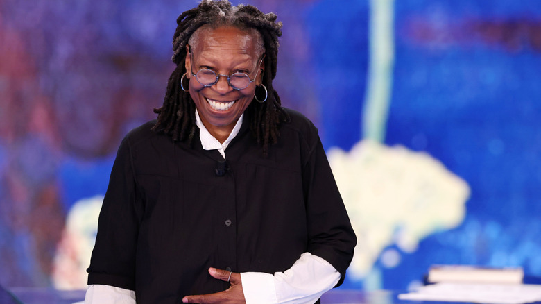 Whoopi Goldberg grinning in a black and white outfit