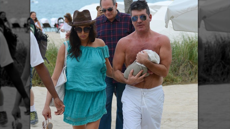 Simon Cowell and Lauren Silverman holding their newborn son while walking at the beach