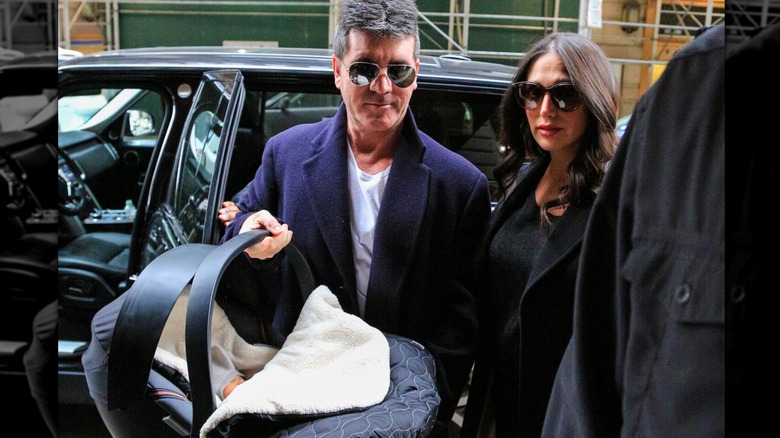 Lauren Silverman and Simon Cowell holding newborn son while exiting car and walking