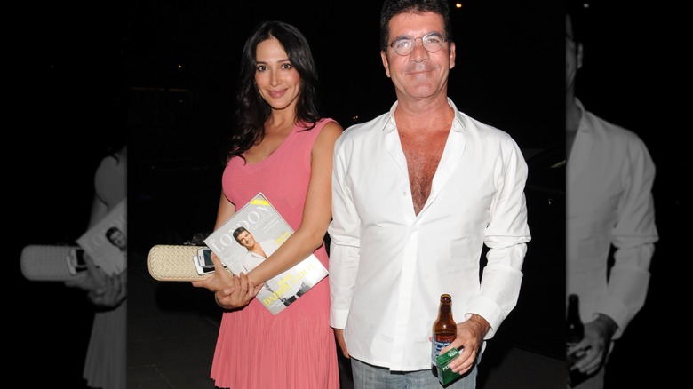 Lauren Silverman and Simon Cowell smiling for a photo while holding magazine and beer