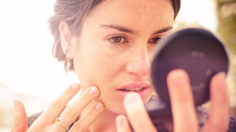 woman checking face in compact mirror