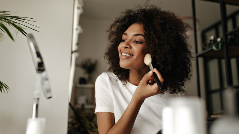 Model smiling applying makeup with brush