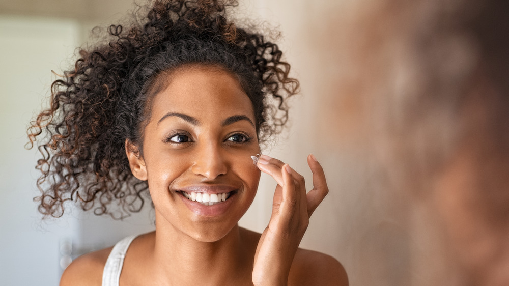 A smiling woman applying lotion to her face