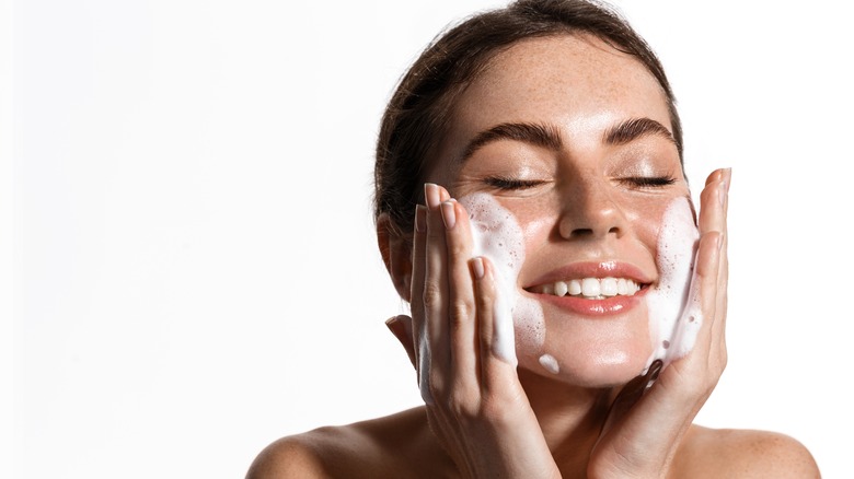 A smiling woman washing her face 