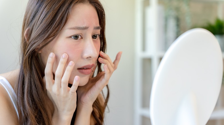 woman looking at skin in mirror