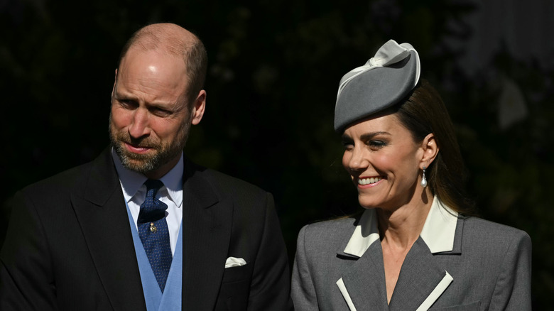 Prince William and Kate Middleton smiling at something off camera in formal wear, slightly squinting from the sun