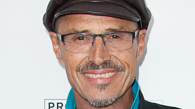 Soap star Michael Nader poses with a smile wearing glasses and a leather hat. 