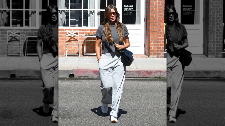 Sofía Vergara in LA in September 2025 wearing light grey track pants, a dark grey t-shirt, white sneakers, sunglasses, and wearing a black crossbody bag