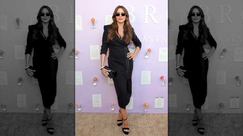 Sofía Vergara at Raising Brows LIVE in 2025 in Los Angeles, California wearing a black jacket-cut dress with black open-toed heels, black sunglasses, silver accessories, and a black clutch bag