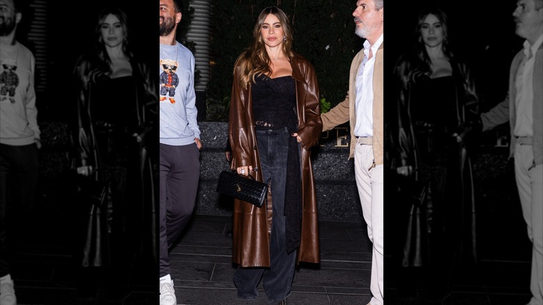 Sofía Vergara at Hudson Yards on October 13, 2024 wearing a black top, dark wash jeans, and a brown leather trench coat while holding a black pocketbook