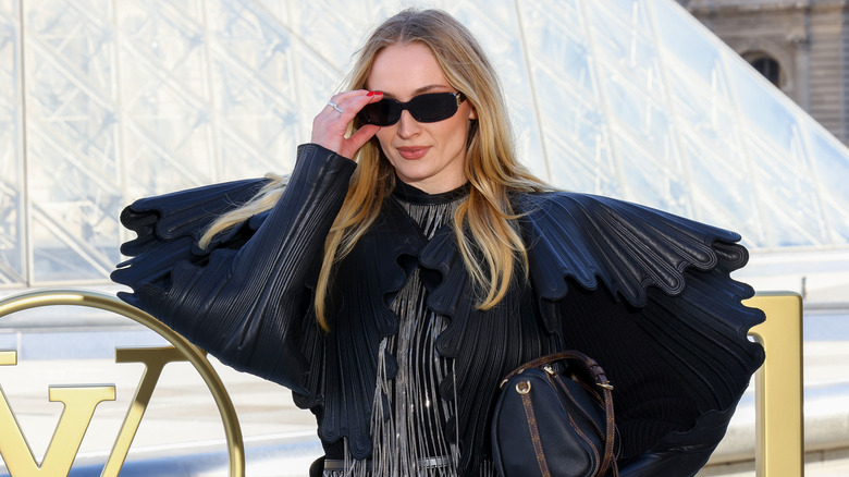 Sophie Turner wearing sunglasses and a black top with wings
