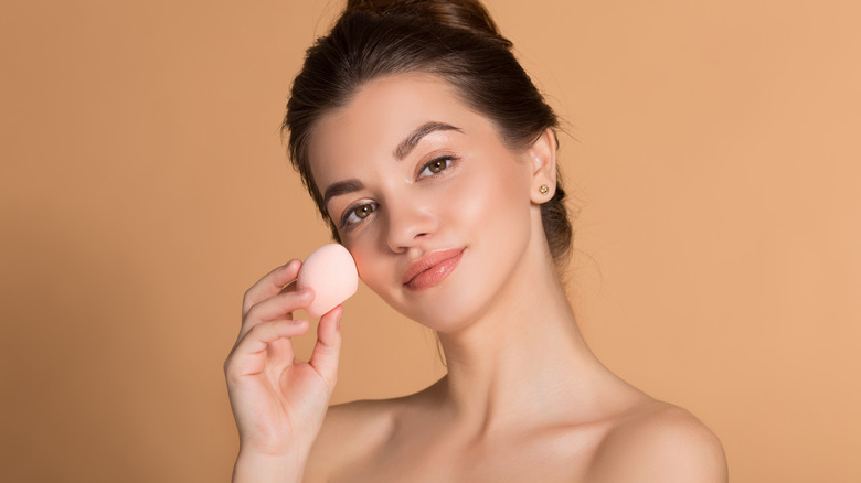 Woman applying makeup with a beauty blender sponge 