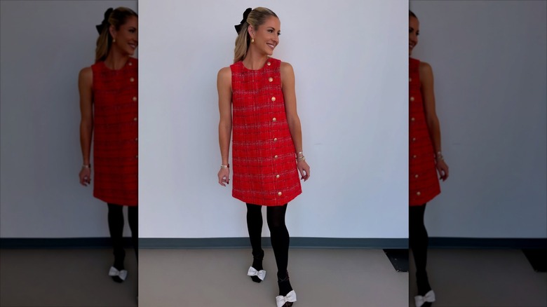 Laura Rutledge in a red dress, looking over her shoulder in front of a white wall.