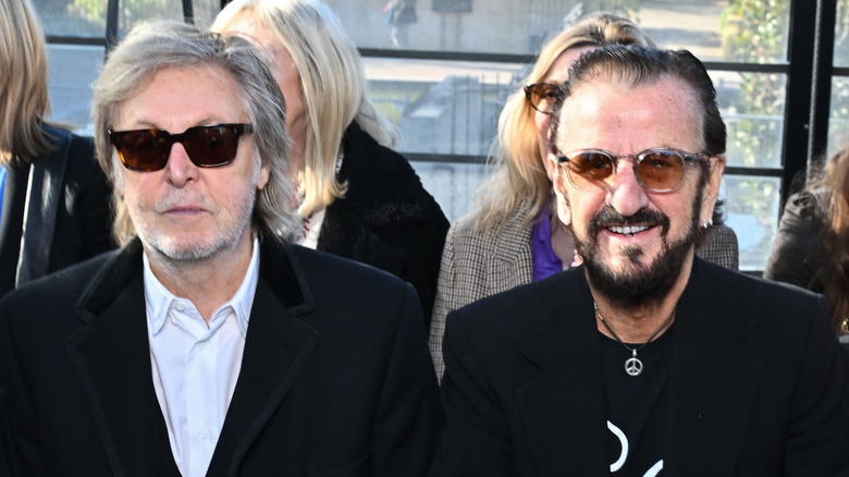 Paul McCartney sitting with Ringo Starr, both wearing sunglasses
